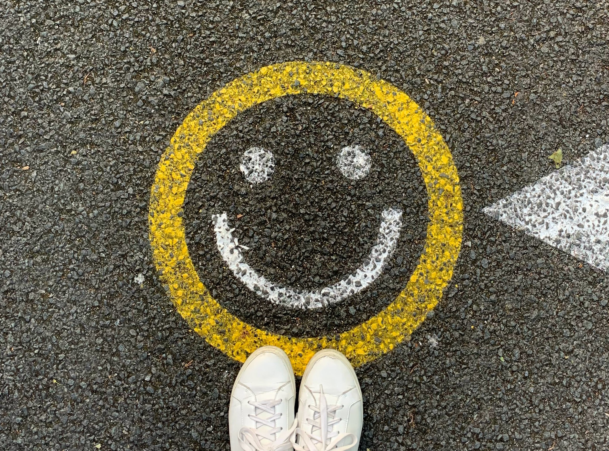 YELLOW CIRCLE WITH WHITE SMILEY FACE INSIDE PAINTED ON ROAD.