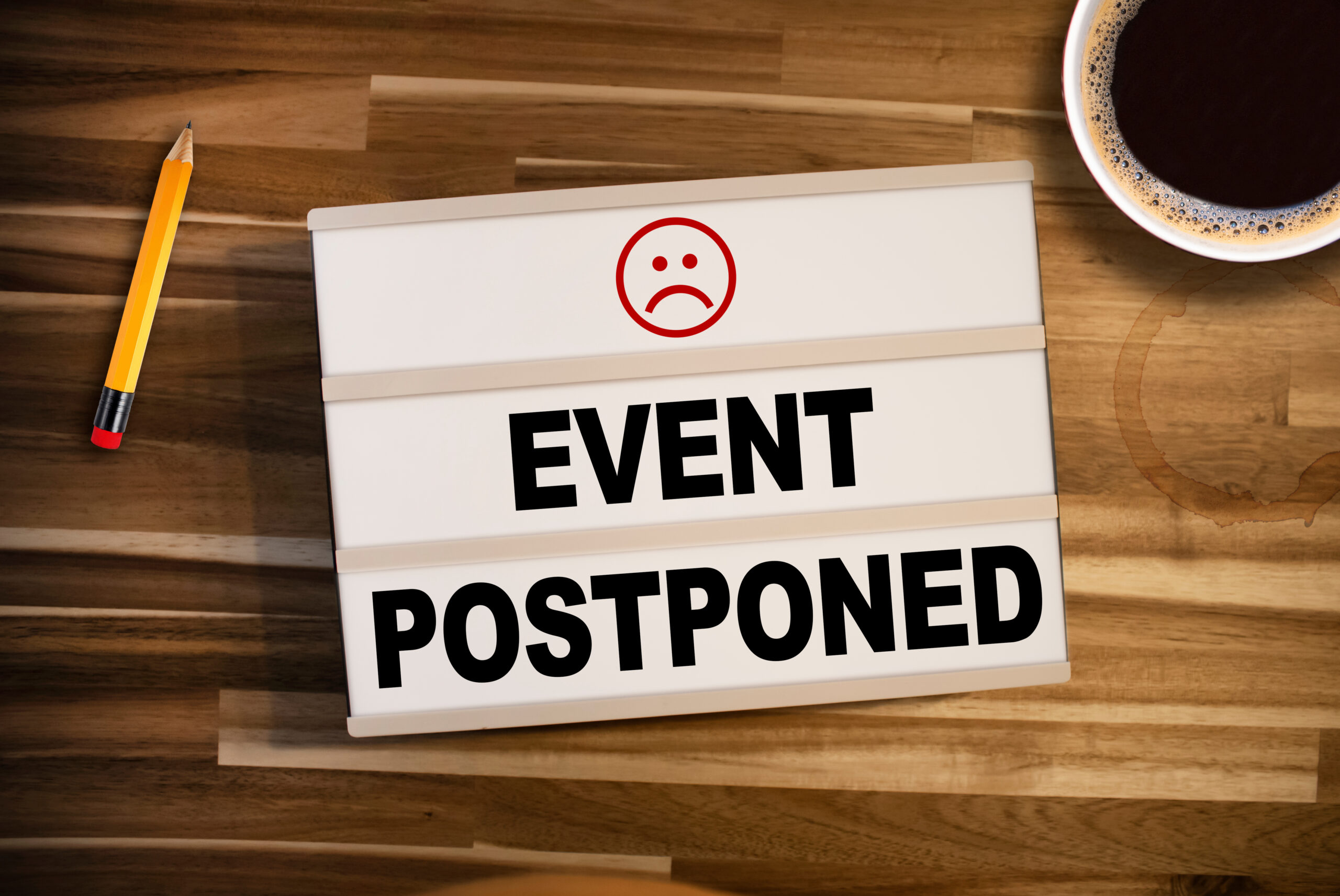 image of a lightbox with the message "event postponed" with a sad face, against a wood background.