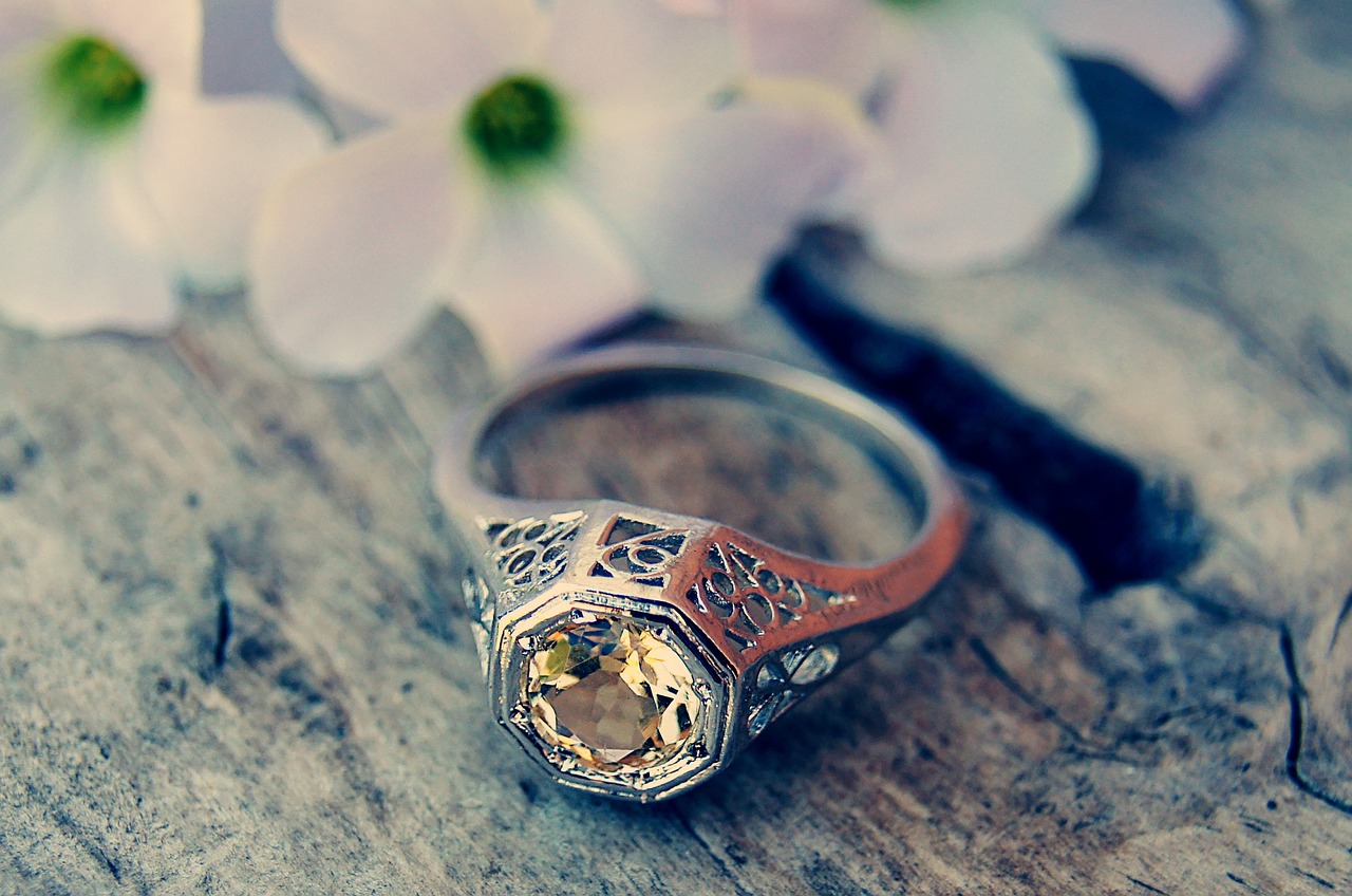 ring with big light green gemstone with white florals in the background on a wood surface